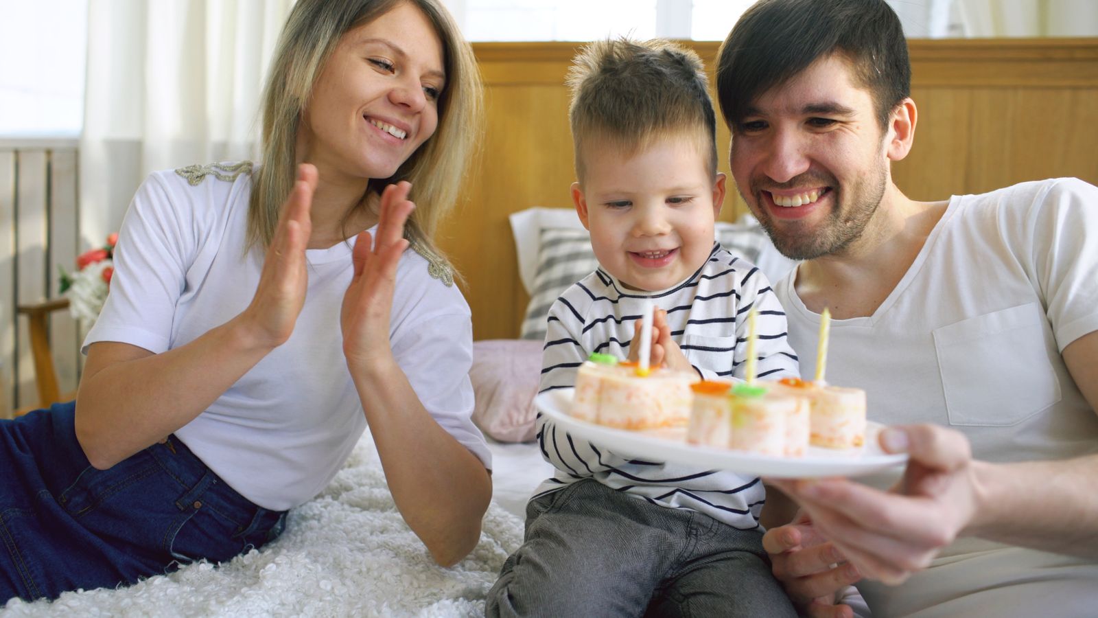 Two parents lean toward a smiling child beside a birthday cake with lit candles.