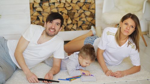 Free Family lounging indoors with child drawing pencils, enjoying relaxation and togetherness. Stock Photo