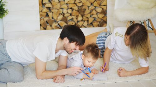 Free Happy family of three drawing together on a cozy rug at home, enjoying quality time. Stock Photo