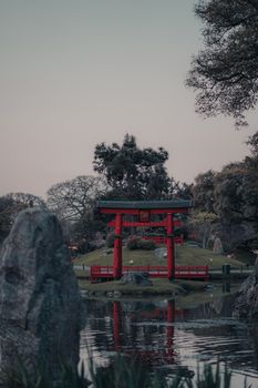 A tranquil view of a red Torii gate in a Japanese garden with reflections in the pond at dusk.