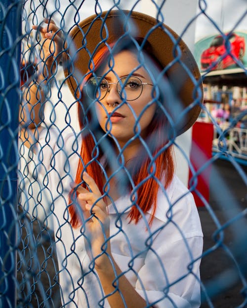 Free Woman Wearing White Collared Top and Beige Hat Behind of Blue Cyclone Fence Stock Photo