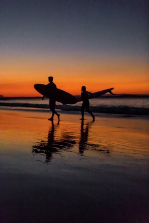 Twee Surfers Aan De Kust Tijdens Zonsondergang