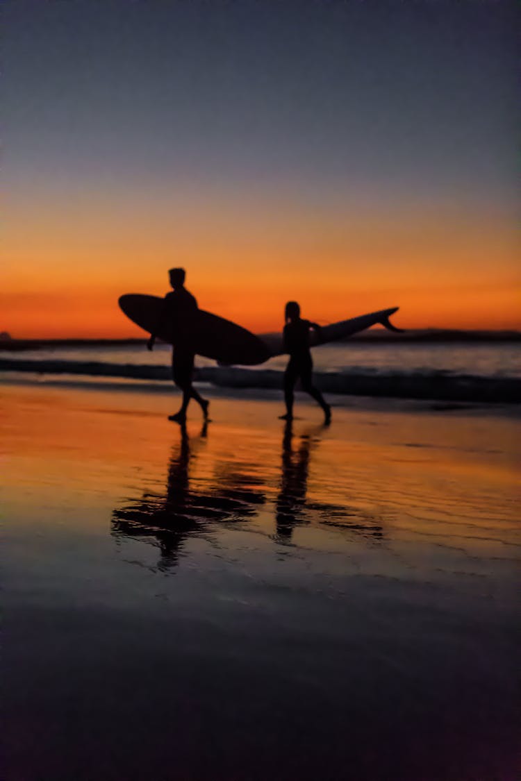 Two Surfers At The Seashore During Sunset