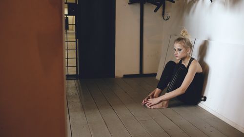 Free A contemplative woman sits barefoot on a wooden floor in a dimly lit room. Stock Photo