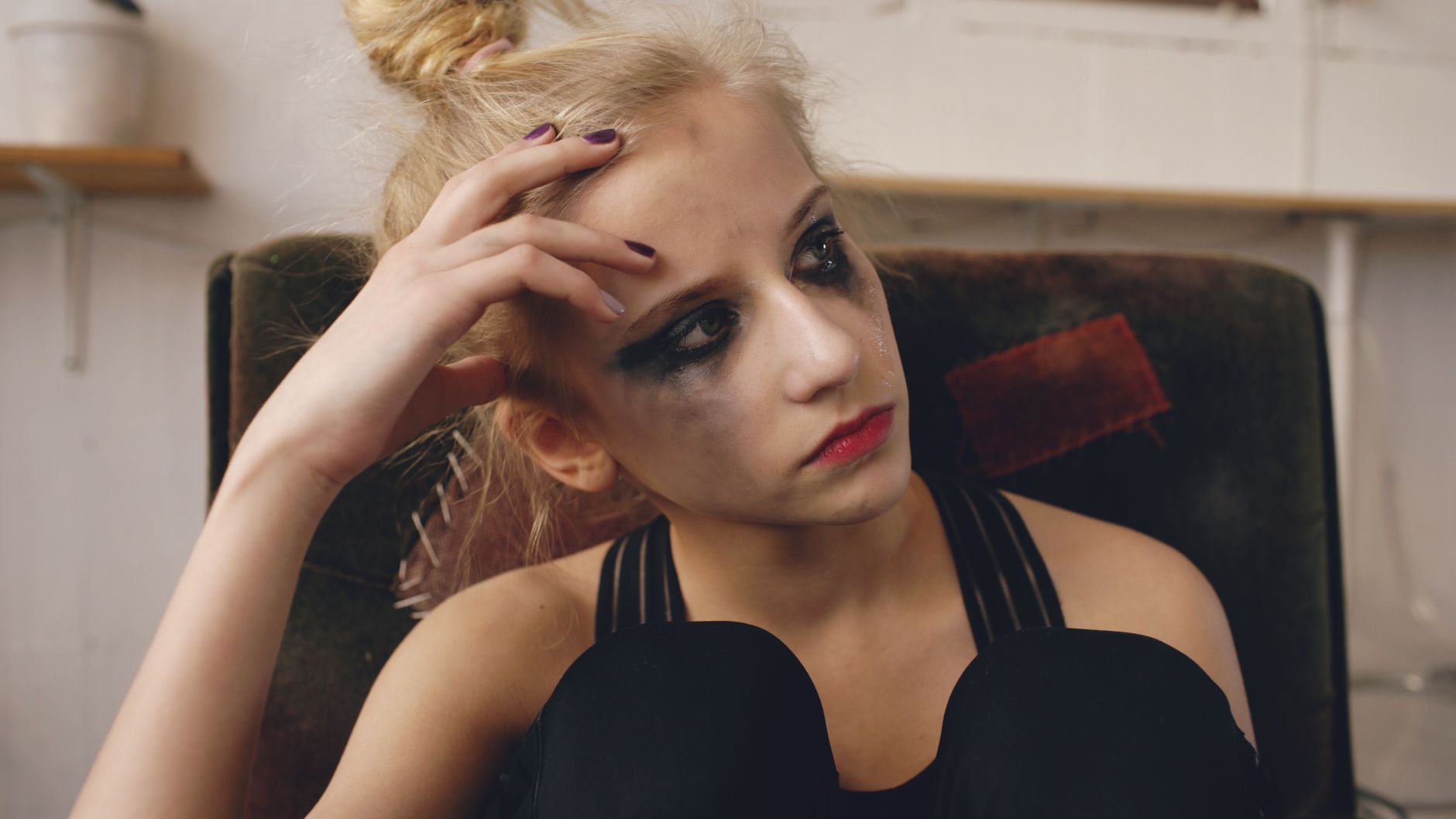 Close-up of a young woman with smudged makeup, expressing sadness and contemplation.