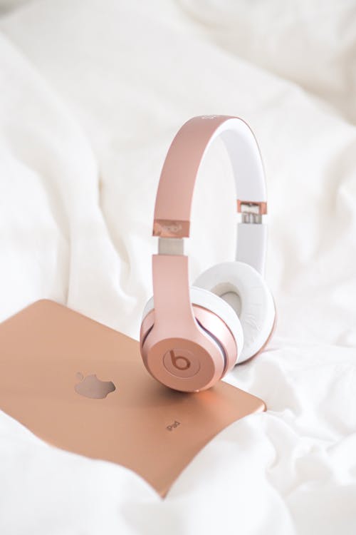 A pair of rose gold headphones on a white bed