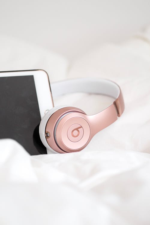 A pink pair of headphones sitting on top of a white bed