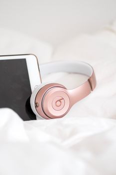 Rose gold headphones resting on a tablet against a cozy white background.