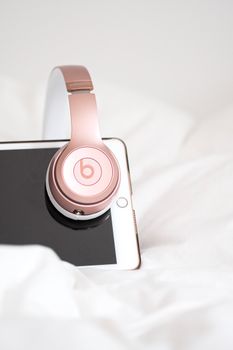 Chic rose gold headphones on a tablet with white background, conveying elegance and technology.