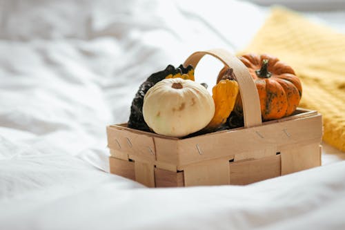A basket filled with pumpkins and squash on a bed