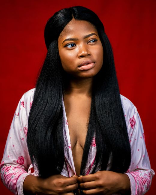 Elegant portrait of a black woman with long hair posing against a red background in a studio.