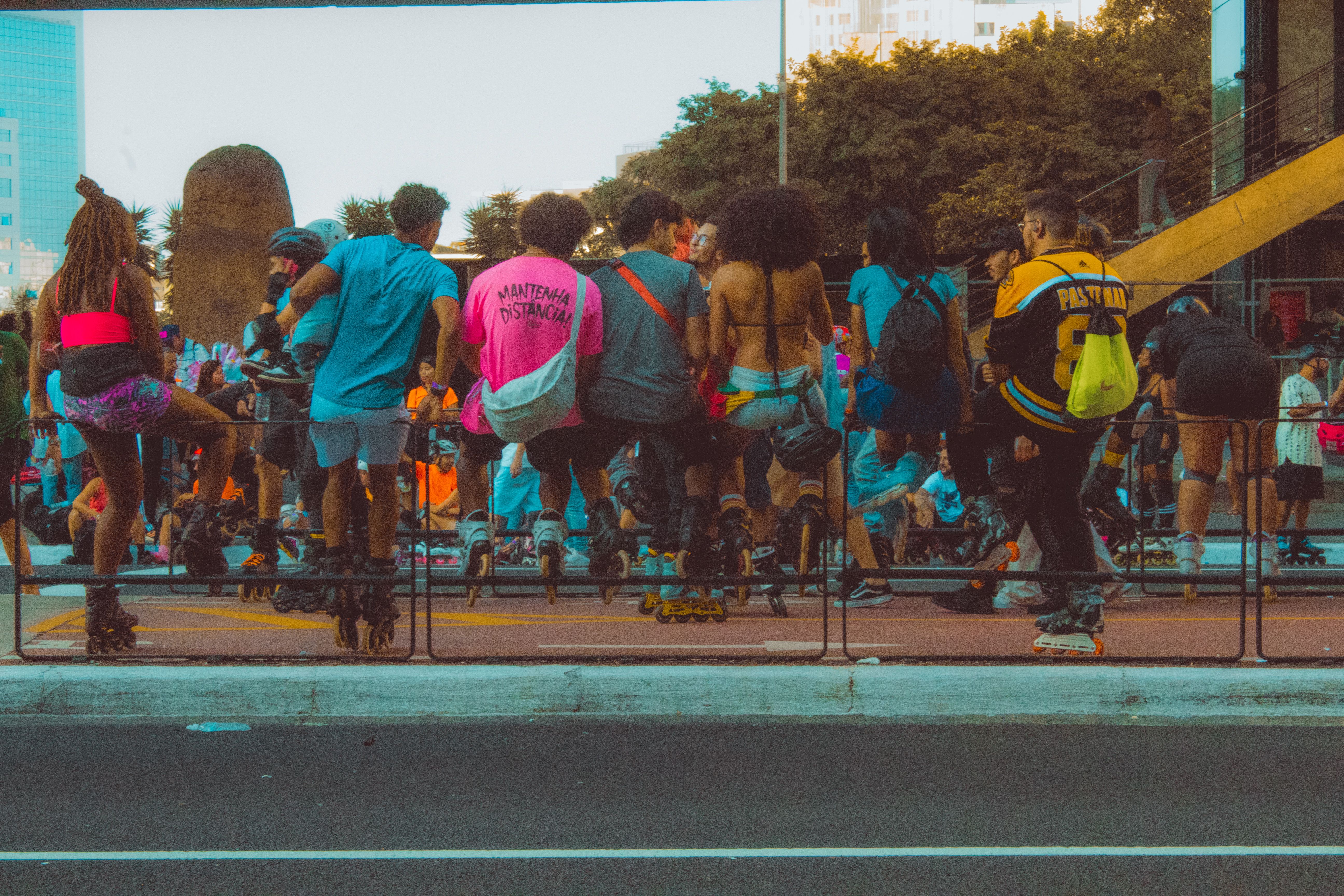 A diverse group of skaters sitting and socializing on a city street railing.