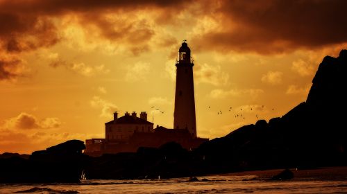 Free Silhouette of a lighthouse against a dramatic sunset sky over the ocean. Stock Photo