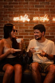 Happy couple enjoying coffee at a café with a cozy ambiance and neon lights.