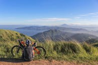 一名山地自行车手停下休息，在明亮的蓝天下欣赏郁郁葱葱的山丘和远处的水面