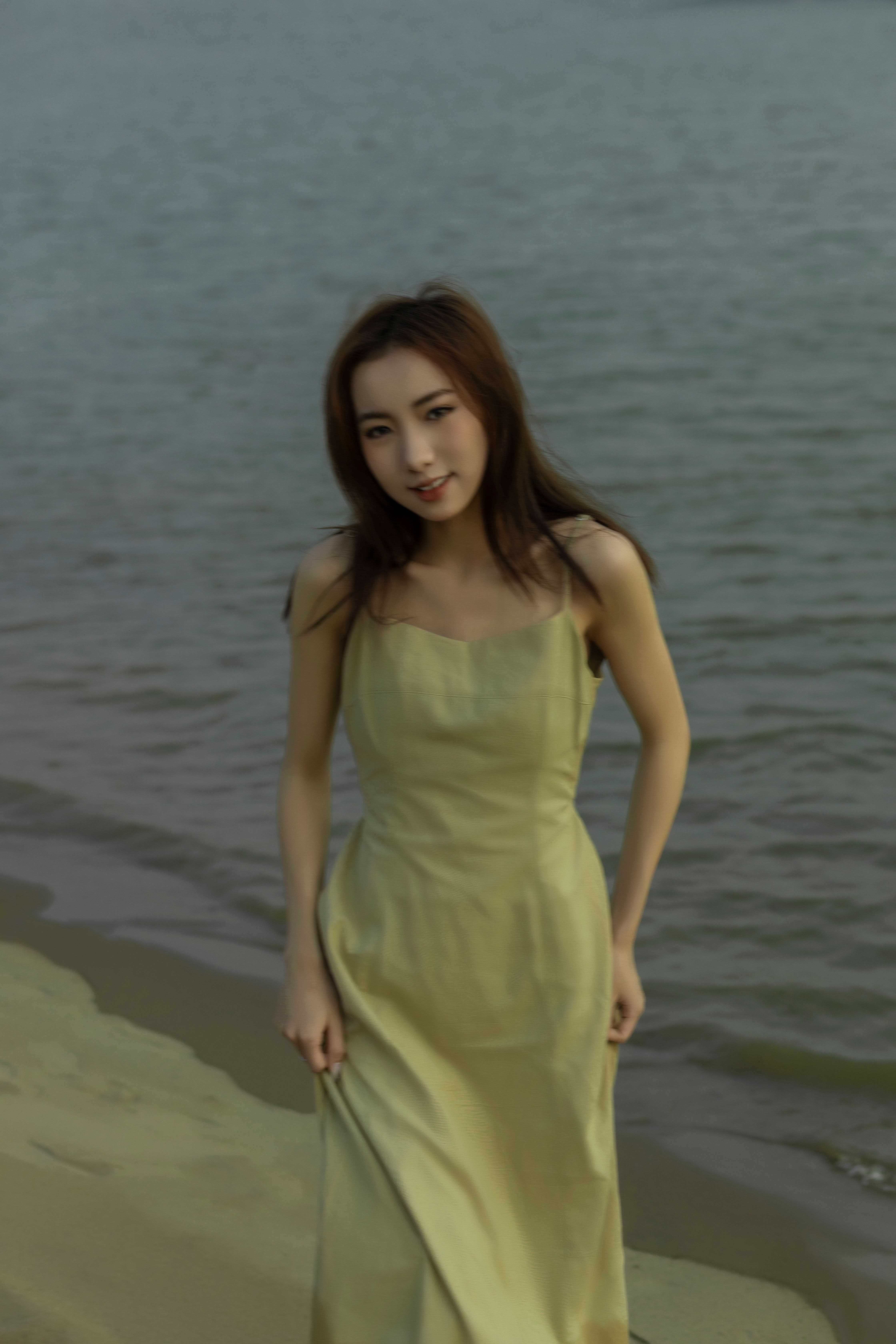 Beautiful Asian woman in a yellow dress posing gracefully on a sandy beach by the sea.