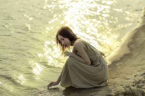 A woman in a dress kneeling on the beach