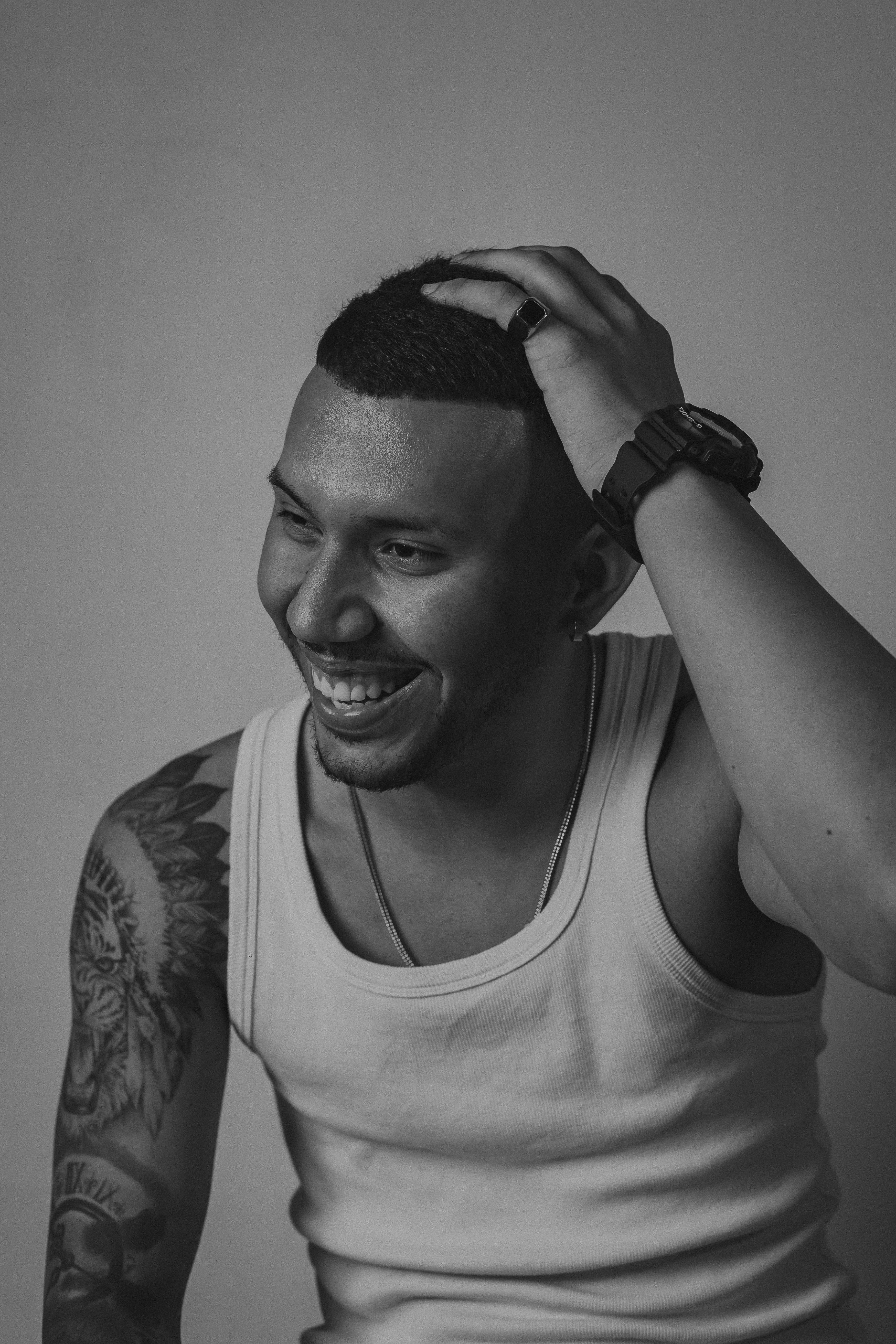 Striking black and white portrait of a smiling man with tattoos in a studio setting.
