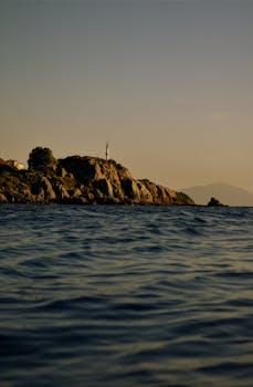 Serene seascape with a distant rocky shoreline and minaret at sunset.