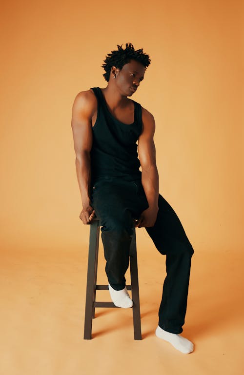 A black man sitting on a stool in a tank top