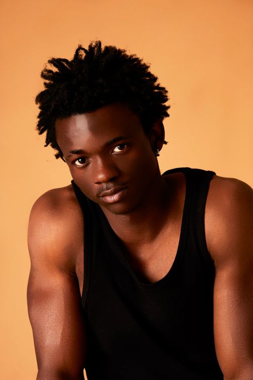Free A muscular black man in a black tank top posing confidently in a studio setting against a yellow background. Stock Photo