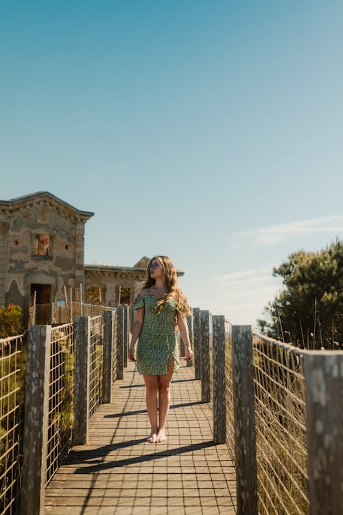 A woman in a green dress walks on a wooden bridge