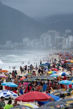 A bustling beach day with vibrant umbrellas on Ipanema Beach, Rio de Janeiro, despite looming storm clouds.