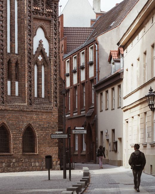 A scenic view of a historic street in Berlin with people walking and iconic architecture.