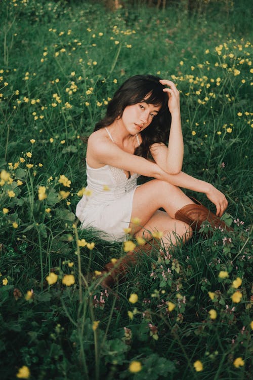 Young Woman in a White Dress and Boots Sitting on a Meadow 