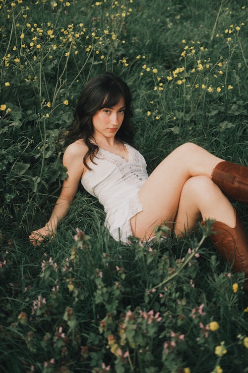 A woman in white dress and cowboy boots sitting in a field