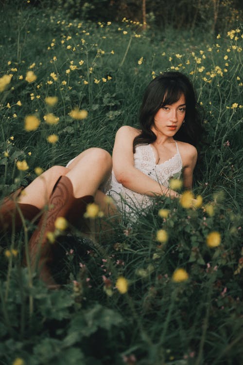 A woman in a white dress and cowboy boots sitting in a field of flowers