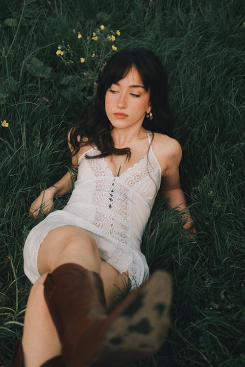 A woman laying in the grass wearing a white dress