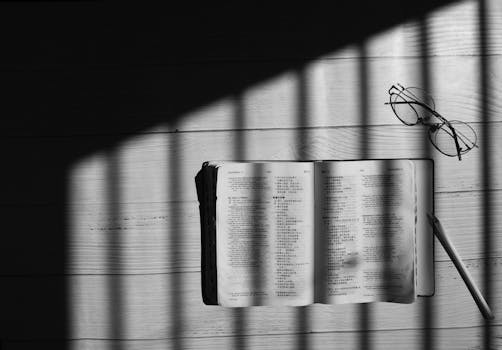 Open book with eyeglasses and pencil casting shadows in black and white.