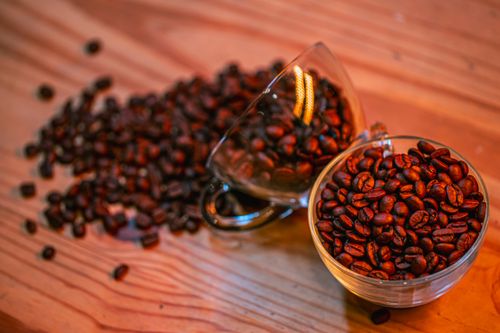 Free Close-up of rich brown coffee beans spilled from glass cups onto a wooden table. Stock Photo