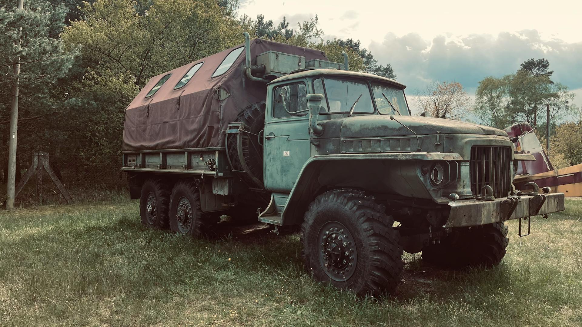 An old army truck with a covered back parked outdoors, surrounded by trees.