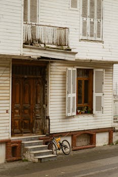 A vintage urban building with wooden shutters, classic architecture, and a bicycle parked by the entrance.