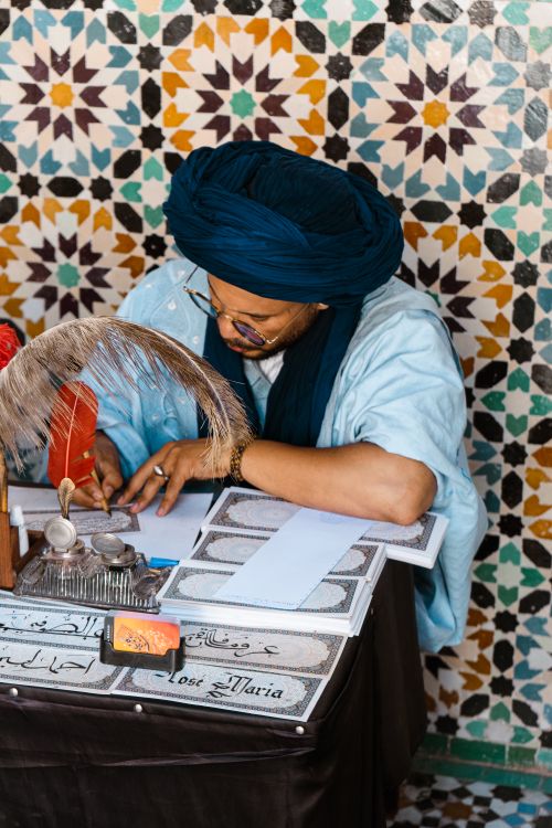 Free A Moroccan calligrapher writes using traditional tools against a mosaic wall. Stock Photo