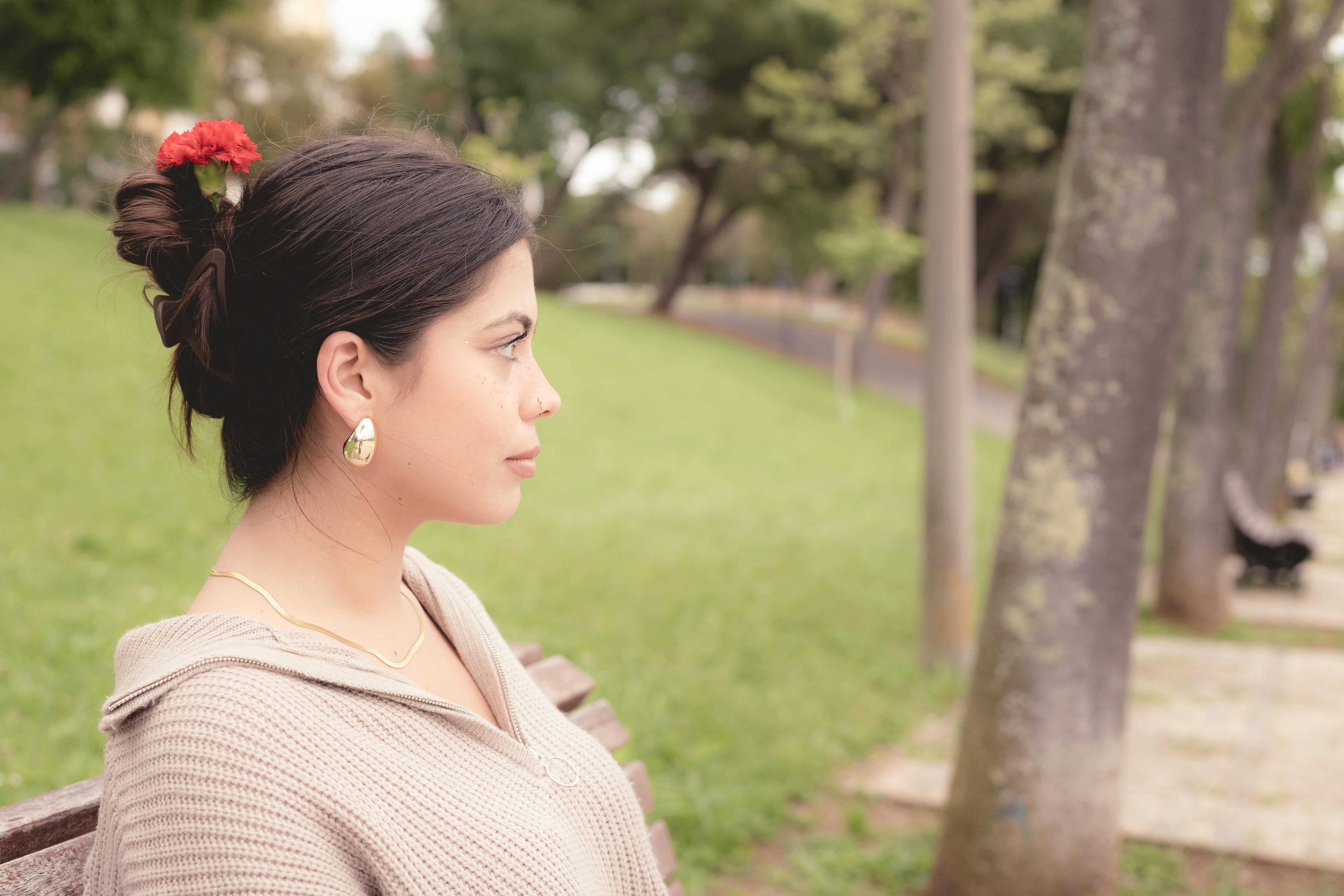 A serene side profile of a woman with a red floral hairpin, sitting on a park bench.