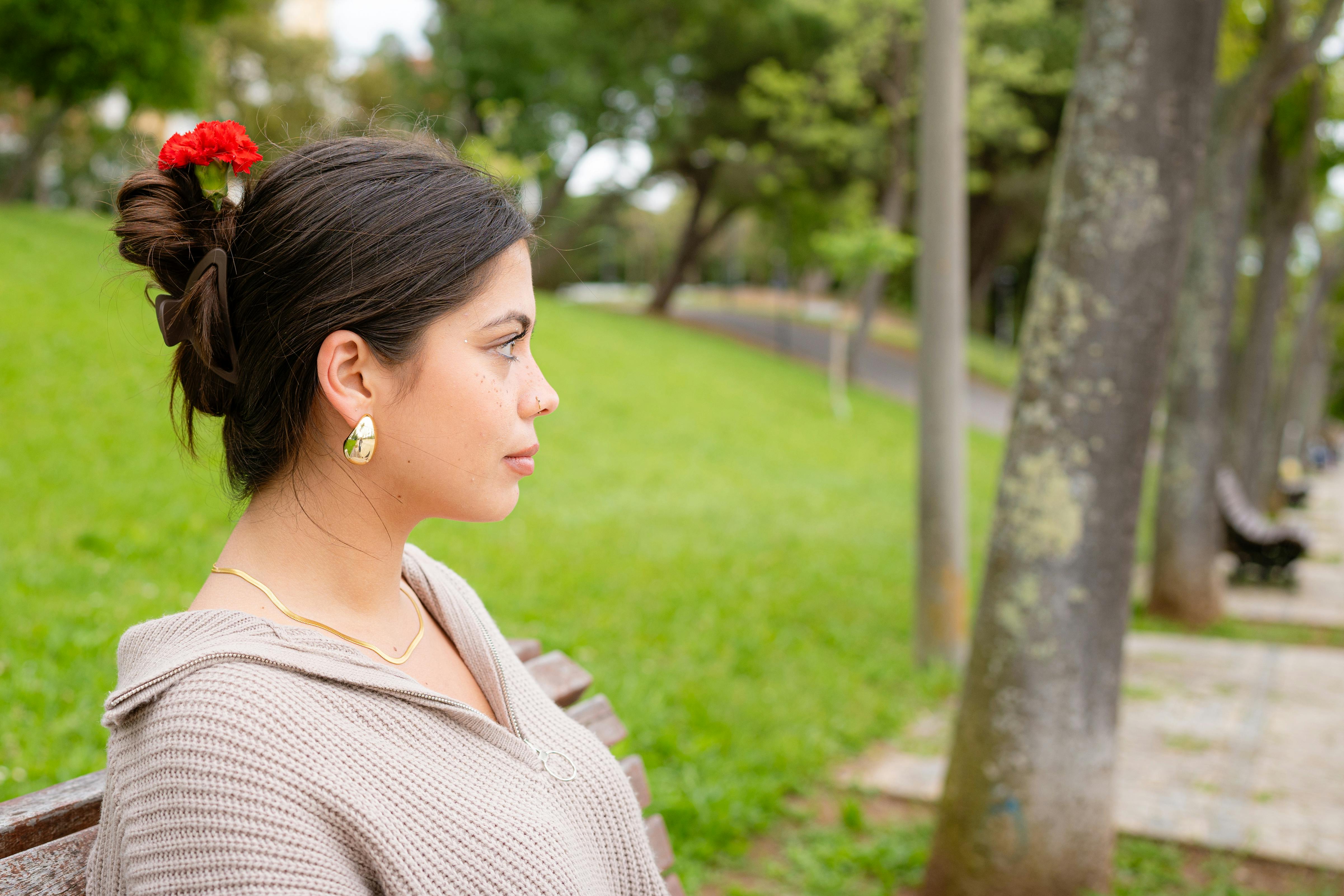 Young woman sitting in a park, enjoying nature with a red flower in hair