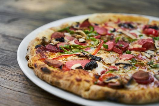 Close-up of a freshly baked pepperoni pizza with mushrooms, peppers, and onions on a wooden table.