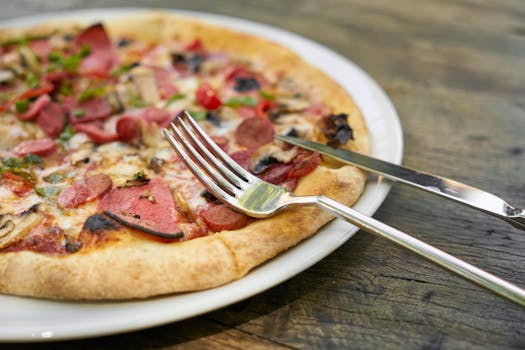 Close-up of a delectable pizza slice with toppings, served on a white plate with cutlery.