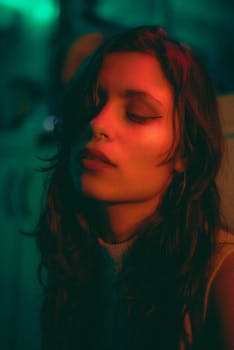 Artistic close-up of a brunette woman bathed in moody neon lighting, eyes closed.