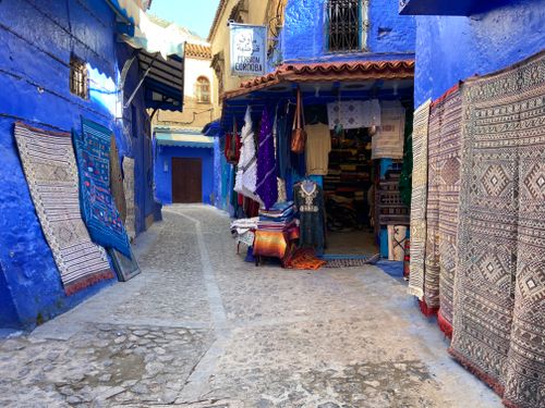 Free Vibrant blue alley with traditional textiles in Chefchaouen, Morocco's medina. Stock Photo
