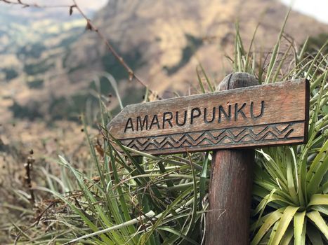 Wooden sign reading 'Amarupunku' in natural landscape near Cusco, Peru.