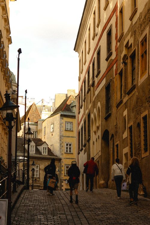 Free A picturesque street in Vienna showcasing historic buildings and people strolling on a cobblestone path. Stock Photo