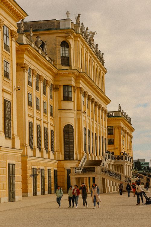 Free Sunlit view of Schönbrunn Palace's Baroque architecture with visitors strolling outside. Stock Photo