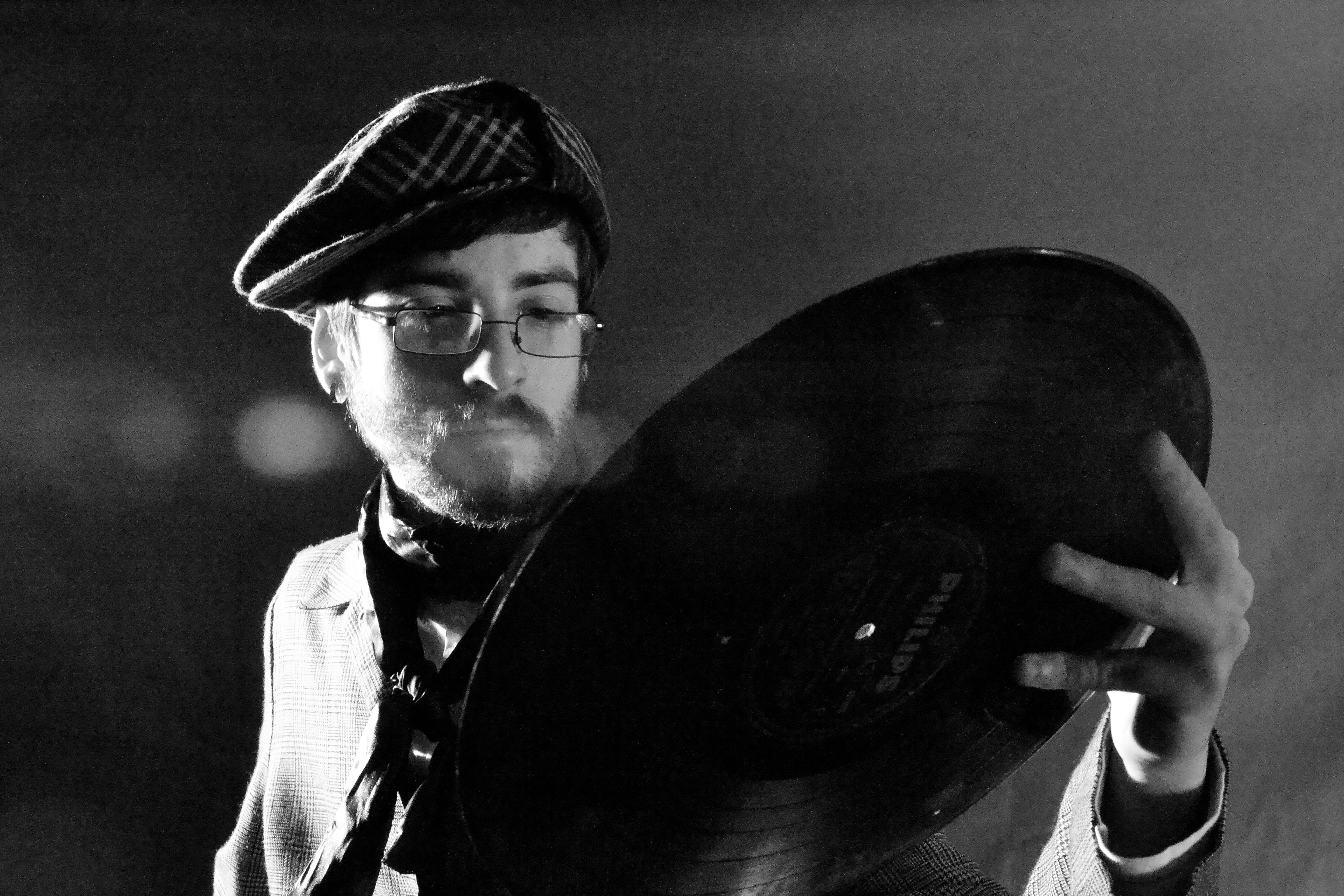 Artistic black and white photo of a man in a beret holding a vinyl record.