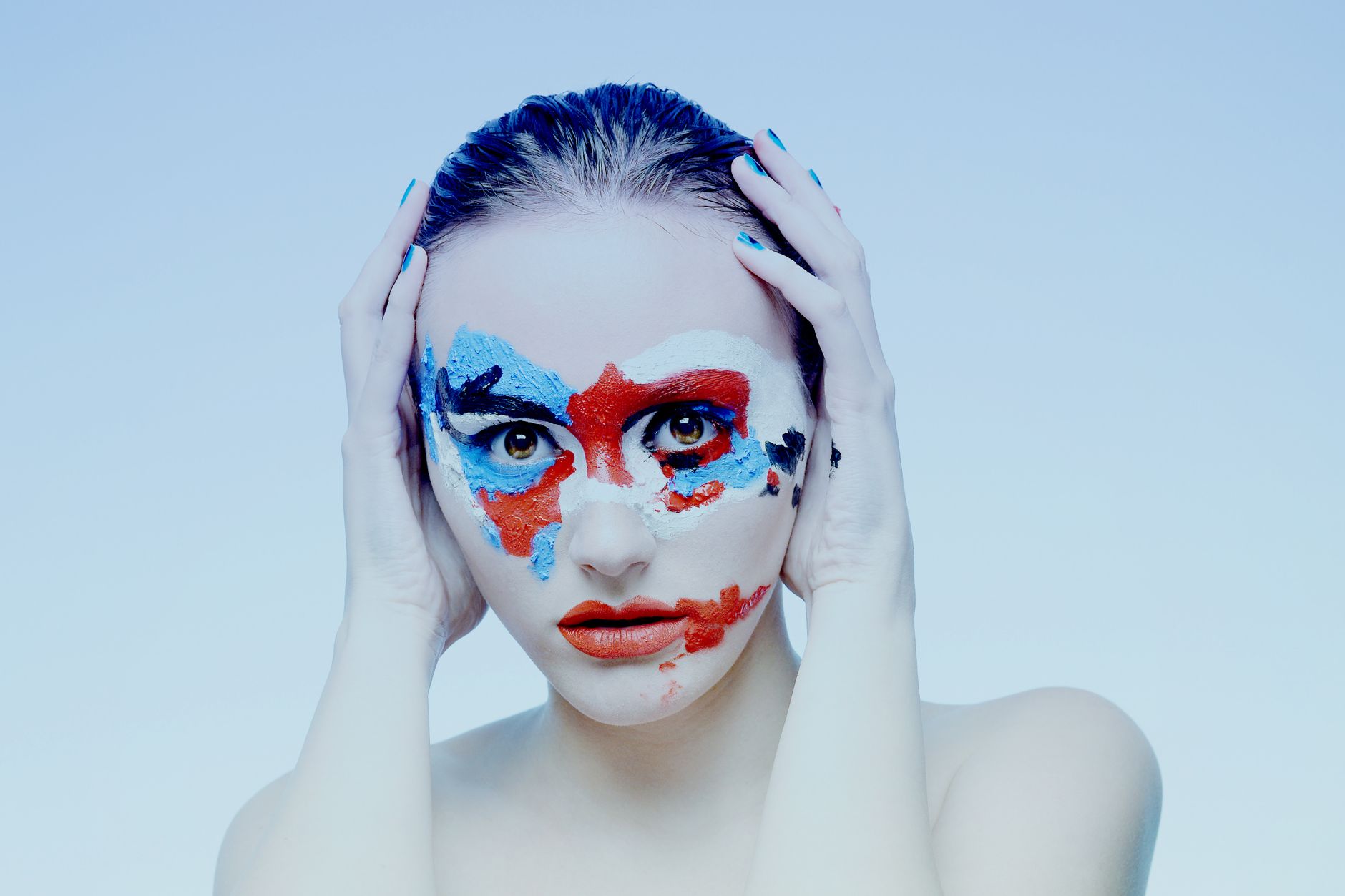 Artistic portrait of a woman with vibrant face paint in studio setting, embodying creativity and expression.