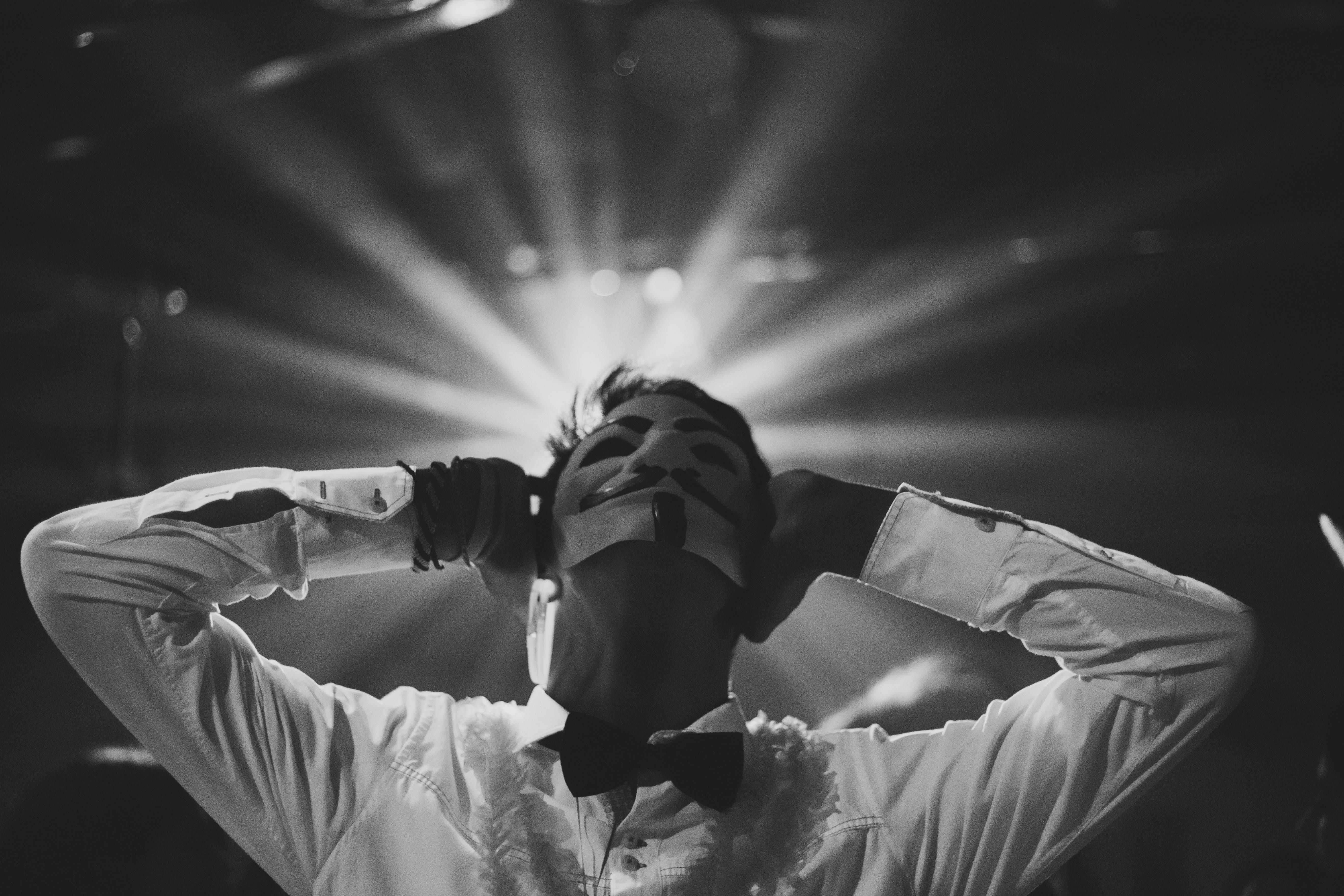 Black and white portrait of a person wearing an elegant mask under spotlight.