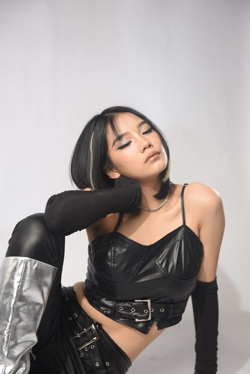 Free Asian woman in a leather outfit posing in a studio with a white background, eyes closed. Stock Photo